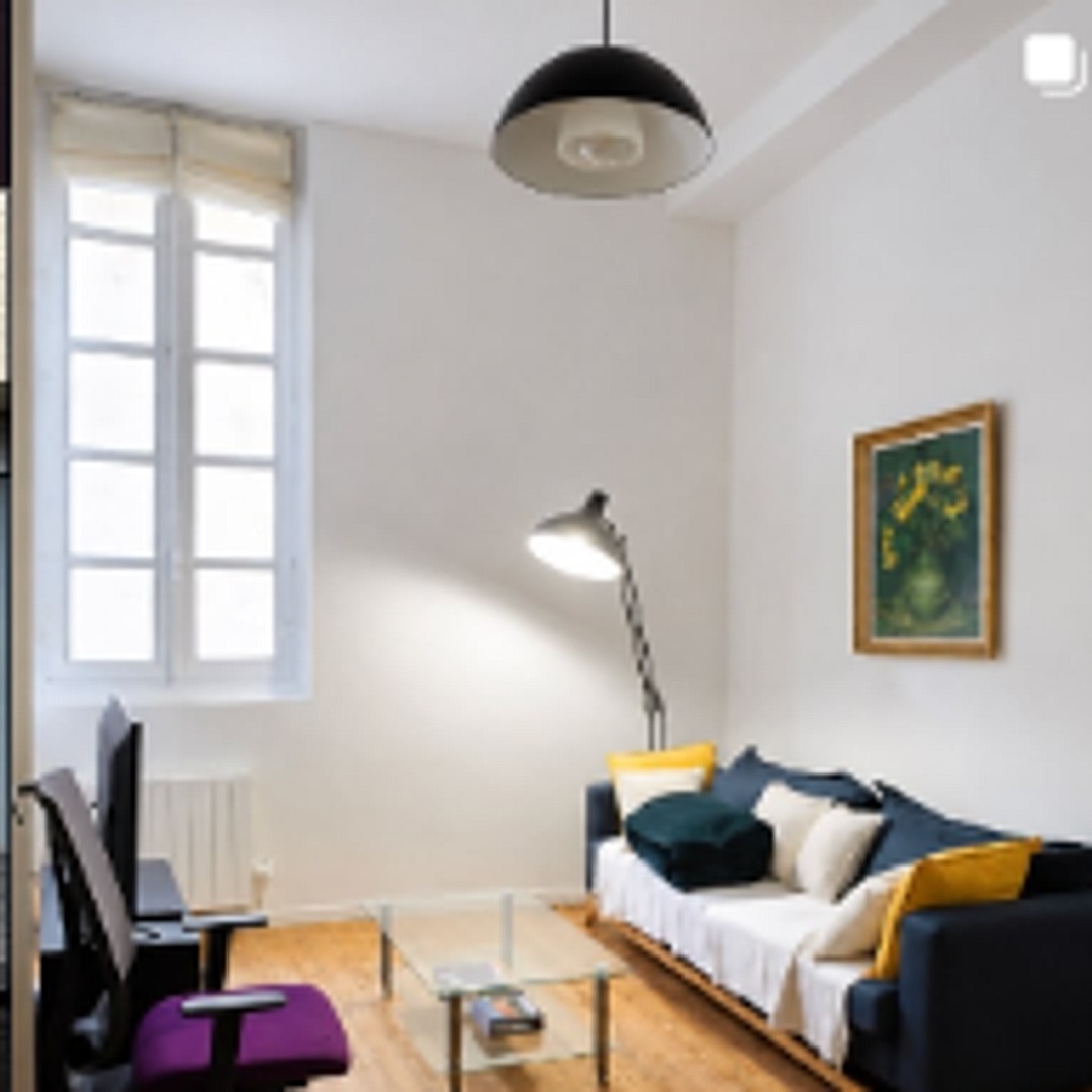 Salon chaleureux baigné de lumière naturelle avec grande fenêtre haussmannienne, parquet ancien et espace bureau dédié pour le télétravail. 🛋️💼